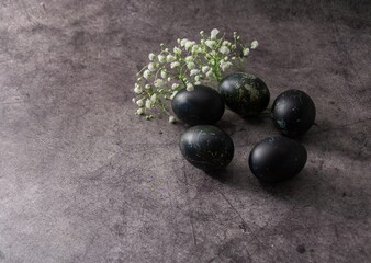Five black colored Easter eggs and wildflowers on a gray surface. Horizontal background for Easter greetings with space for text.