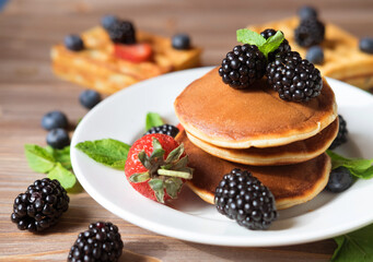 Pancakes with various berry on white plate. Pancakes stack with blueberries, blackberries, strawberries.