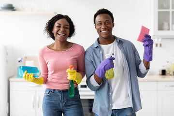 Cheerful black couple with supplies for cleaning posing in kitchen