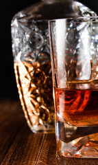 Detail shot of a glass and bottle of whiskey on a wooden table and black background. International whiskey day