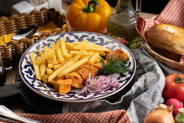 A portion of chicken shish kebab with French fries, onions and dill