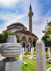 View of Alipasina Mosque in Sarajevo, Bosnia and Herzegovina. In the foreground is a turban tombstone, and the white gravestones in the cemetery garden.
