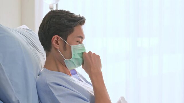 Asian young male patient having a cough, lying on bed in recovery room