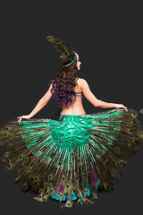 Dancer holds peacock feathers in her hands black background view from the back.