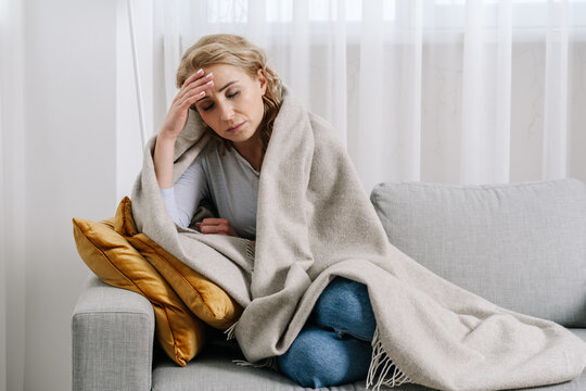 Ill woman covered with blanket sit on sofa