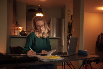 one young woman, working late at night at home at desk. scribbling notes on paper, reading from...