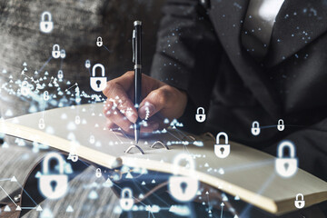 Businesswoman is taking notes of clients needs to protect cyber security from hacker attacks and save clients confidential data. Padlock Hologram icons over the typing hands. Formal wear
