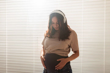 Smiling brunette pacified pregnant woman listening to pleasant music using a smartphone and headphones. Sedation therapy concept before meeting with baby