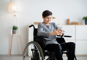 Happy disabled teen in wheelchair using digital tablet at home, browsing internet or watching...