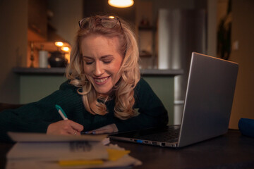 one young woman, smiling. working late at night, writing on her desk some notes.