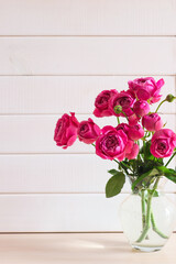 Bouquet of roses close-up in vase against rustic wooden background. Beautiful festive floral card with copy space for congratulations. Selective focus