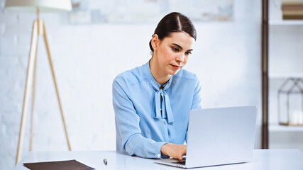 young, serious businesswoman typing on laptop in office