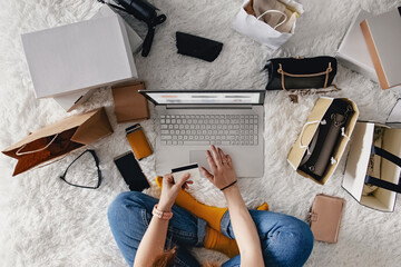 Woman sitting on the bed full of boxes and goods with her laptop buying goods.