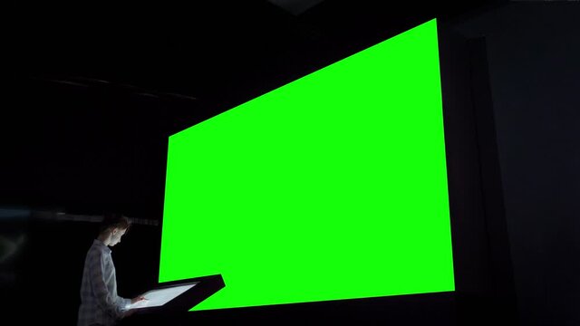 Woman using electronic kiosk and looking at large wall blank green display at science exhibition or cinema. Technology, chroma key, futuristic, template, mock up, green screen, entertainment concept