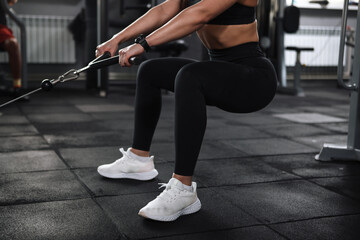 Cropped shot of unrecognizable sportswoman with toned sexy body squatting in crossover gym machine