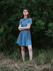 A woman in a blue dress near a green bush with red berries in full growth