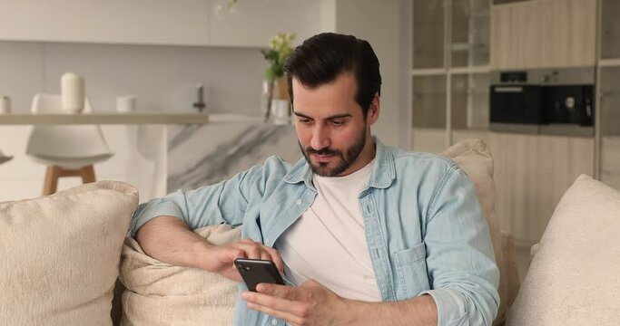 Young attractive man spend weekend at home using smartphone device, texting sms, share messages to friends in social media network feel happy, enjoy free time, online fun and modern tech usage concept