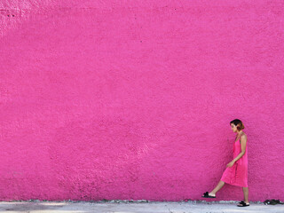 Girl in pink dress walking against pink wall.