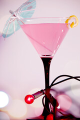 pink cosmopolitan cocktail with lemon peel and colourful string lights