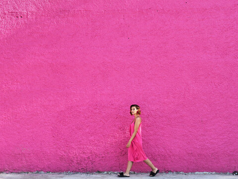 Girl in pink dress walking against pink wall.