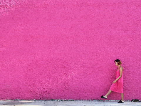 Girl in pink dress walking against pink wall.