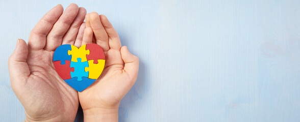 Father and autistic son hands holding jigsaw puzzle heart shape. Autism spectrum disorder family support concept. World Autism Awareness Day