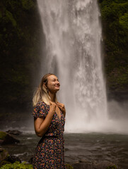 Happy woman smiling and enjoying waterfall landscape. Nature and environment concept. Travel lifestyle. Woman wearing dress. Copy space. Nung Nung waterfall in Bali