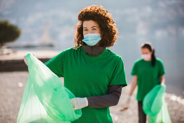  Female volunteers clean beach from garbage, plastic, hold trash bags and care of environment.