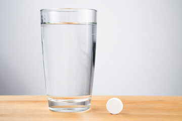 Close up sparkling water glass with dissolving effervescent aspirin pill standing on wooden table, sick unhealthy woman taking emergency medicine