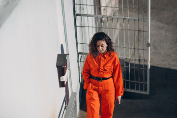 Young prisoner woman in orange suit at jail smoking. Female in colorful overalls portrait.