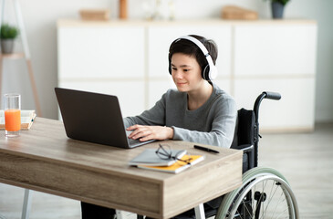 Disabled teen boy listening to music while doing online homework on laptop, indoors
