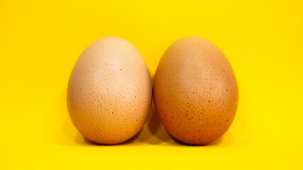 Two identical eggs of different shell colors on a yellow background.