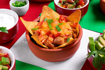 Nachos with chicken, mushroom and melted cheese in portion bowl served with toppings on geometric background. Mexican food