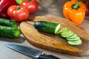 Female hands cutting cucumber on wooden board, close-up, on wooden background