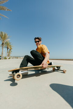 Young man skateboarding with a longboard in front of the beach