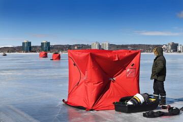 Barrie, Ontario, Canada - March 7, 2021: Fisherman erecting a red ice fishing tent on frozen Kempenfelt Bay of Lake Simcoe in winter