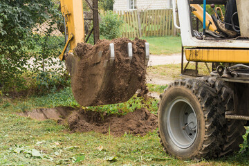 Excavation work on the construction site. A bucket of a bulldozer digs the ground with a grass...