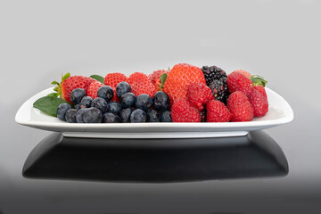 Berries in the foreground on white plate. Strawberries, raspberry, blackberries and blueberries with green leaves