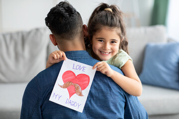 Father's Day Concept. Smiling little girl embracing dad and holding greeting card