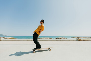 Young man skateboarding with a longboard in front of the beach