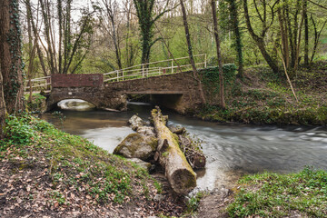A tree trunk in the Angerbach with the footbridge in the background, seen near Ratingen, North Rhine-Westphalia, Germany