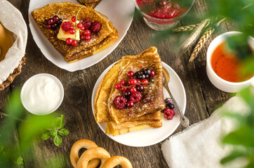 Obraz na płótnie Canvas Pancakes with berries with tea, sour cream for the Russian holiday Maslenitsa on a wooden background flat lay