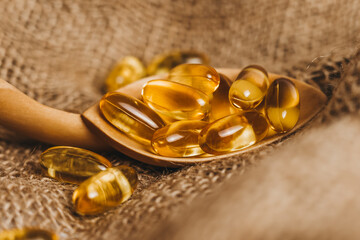 Fish oil capsules on a wooden spoon. Fish oil pills, tablets on the burlap. Vitamin complex omega...