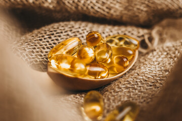 Fish oil capsules on a wooden spoon. Fish oil pills, tablets on the burlap. Vitamin complex omega 3,6,9. Fish oil capsules with omega-3, vitamin D. Close up