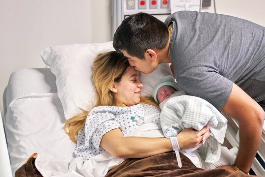 Newborn baby: Father of newborn kissing the mom in the hospital bed with family's baby newborn