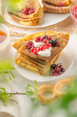 Pancakes with berries and sour cream for the Russian Maslenitsa holiday on a white background with bokeh of greens