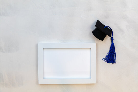 White Frame Mockup With Graduation Cap And Royal Blue Tassle On Gray Wash Background Flat Lay Copy Space