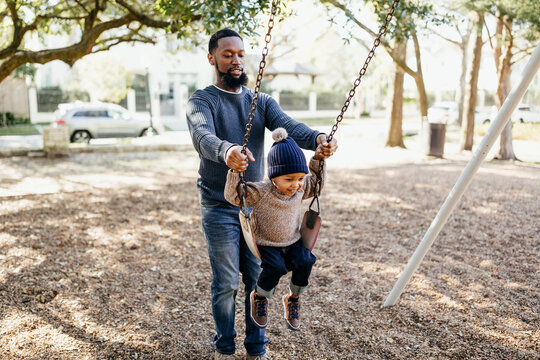 An adorable little boy on a park swing with his dad