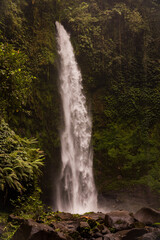 Fototapeta na wymiar Waterfall landscape. Beautiful hidden waterfall in tropical rainforest. Foreground with big stones. Slow shutter speed, motion photography. Travel and adventure. Nung Nung waterfall, Bali