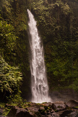 Obraz premium Waterfall landscape. Beautiful hidden waterfall in tropical rainforest. Foreground with big stones. Slow shutter speed, motion photography. Travel and adventure. Nung Nung waterfall, Bali